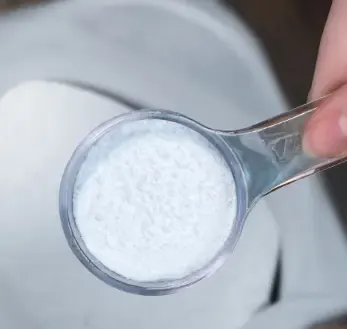 A measuring scoop of white magnesium BHB powder over a bowl